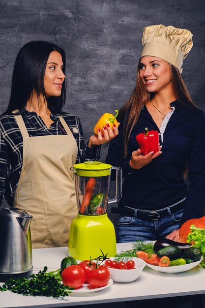 Zwei attraktive junge Frauen, die veganen Gemüsesaft mit Mixer zubereiten.