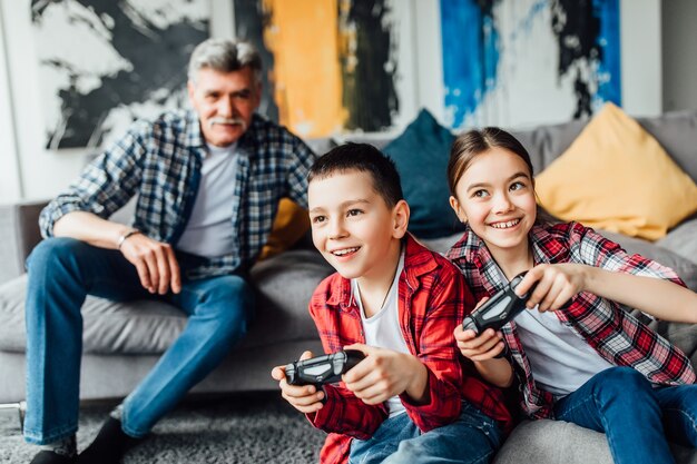 Zwei attraktive Teenager und Mädchen spielen Spielkonsole und lächeln, während sie zu Hause auf der Couch sitzen.