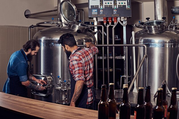 Zwei bärtige Hipster-Männer in einer Schürze, die in der Brauereifabrik arbeiten.