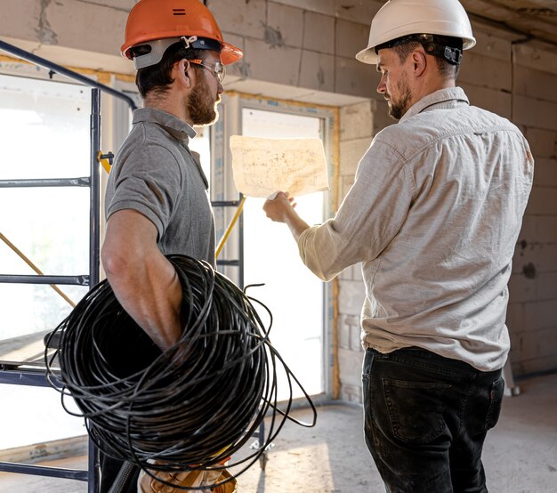 Zwei Bauingenieure sprechen auf der Baustelle, Ingenieur erklärt einem Arbeiter eine Zeichnung