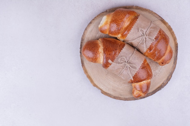 Zwei Croissantbrötchen in Papierverpackung auf Holzbrett.