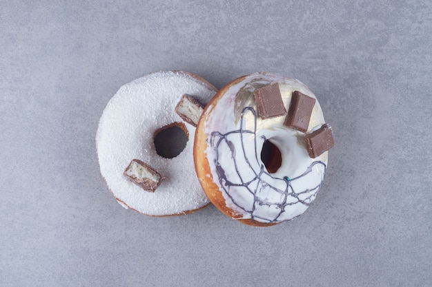 Zwei Donuts mit Schokoladenverzierung auf Marmoroberfläche