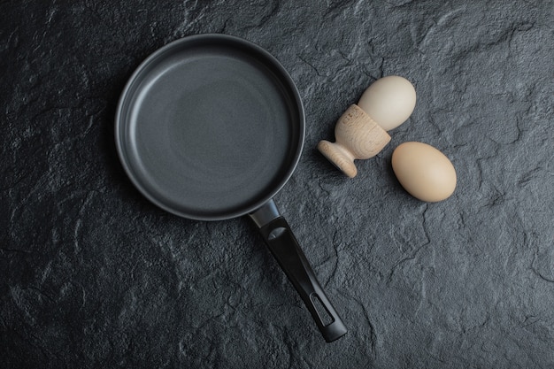 Zwei Ei und schwarze Bratpfanne auf schwarzem Hintergrund.
