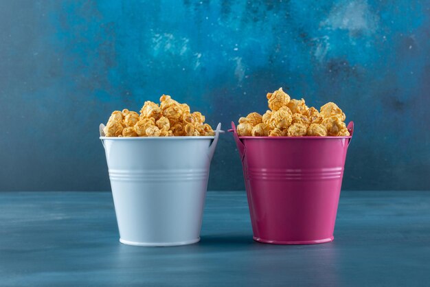 Zwei Eimer gefüllt mit karamellbeschichtetem Popcorn auf Blau