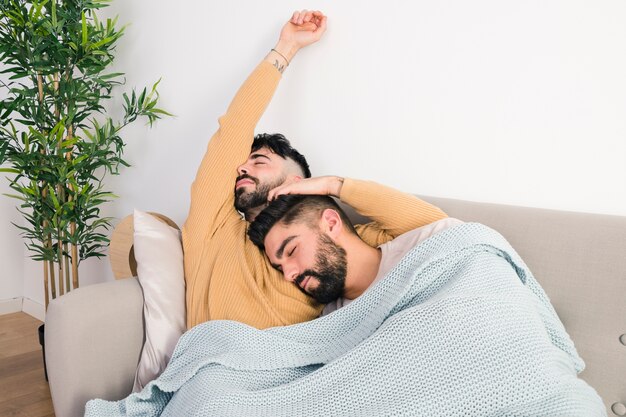 Zwei faule homosexuelle Paare, die auf Sofa in einer Decke liegen
