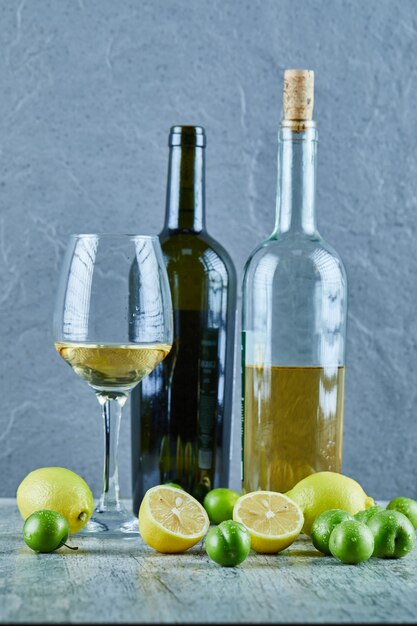 Zwei Flaschen und ein Glas Wein auf Marmortisch mit Zitronen und Kirschpflaumen