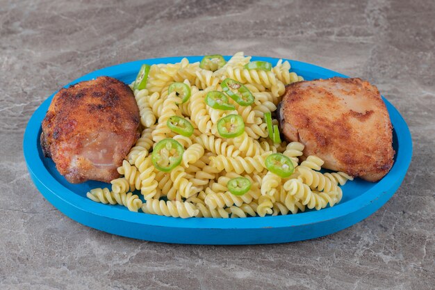 Zwei Fleischstücke und gepfefferte Fusilli-Nudeln auf dem Holztablett, auf der Marmoroberfläche.