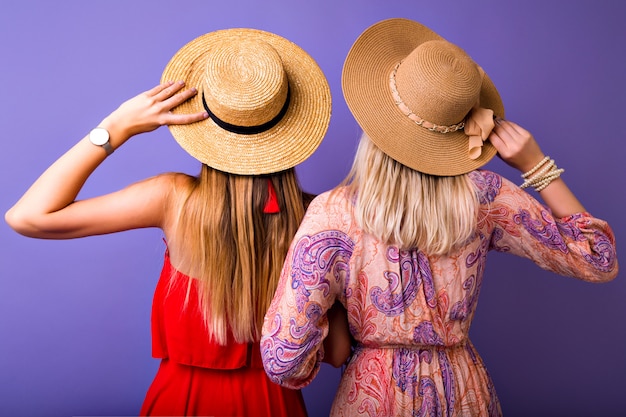 Zwei Frauen bleiben zurück zur Kamera, stilvolle farblich passende Boho elegante Sommeroutfits, Umarmungen und das Tragen von Strohhüten, Modeaccessoires-Konzept.