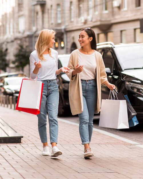 Zwei Frauen, die auf der Straße gehen, während Einkaufstaschen halten