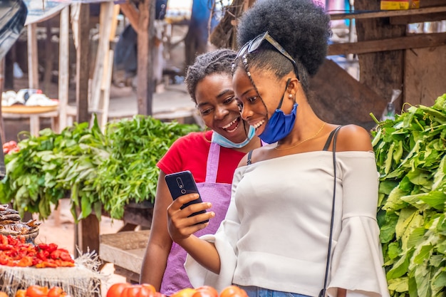 Zwei Frauen, die Inhalt auf einem Telefon in einem lokalen afrikanischen Markt betrachten.