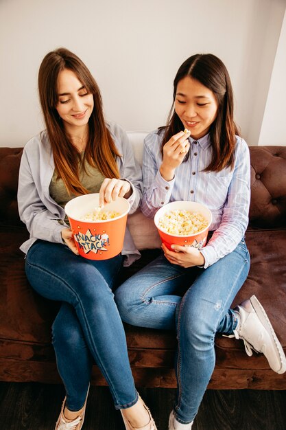 Zwei Frauen, die Popcorn auf Sofa essen