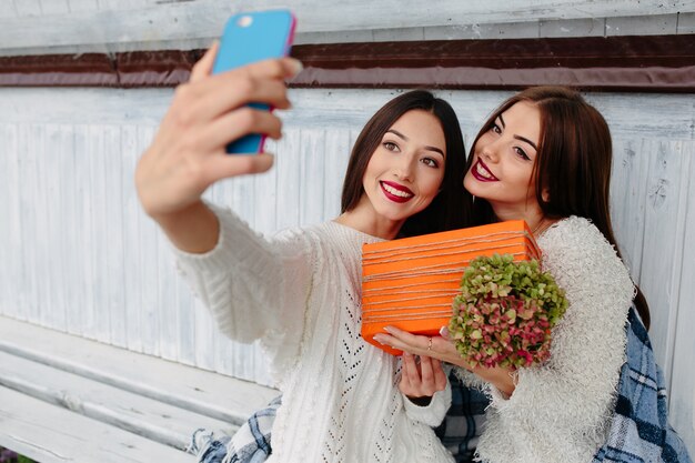 Zwei Frauen sitzen draußen auf einer Bank und machen Selfie mit Geschenk