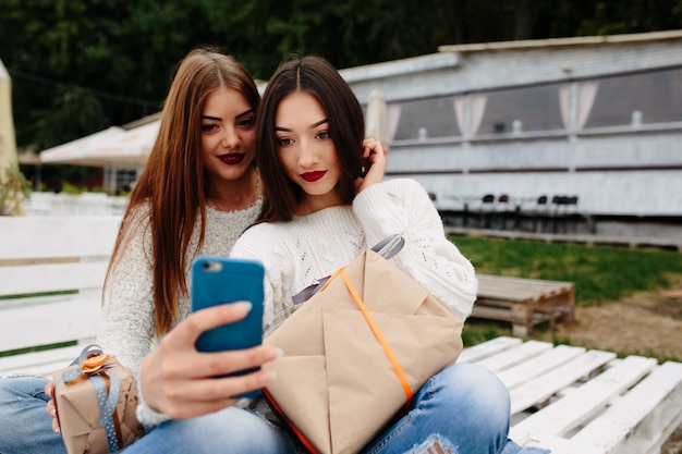 Zwei Frauen sitzen draußen auf einer Bank und schießen Geschenke für das Smartphone