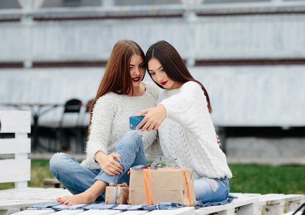 Zwei Frauen sitzen draußen auf einer Bank und schießen Geschenke für das Smartphone