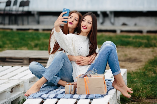 Zwei Frauen sitzen draußen auf einer Bank und schießen Geschenke für das Smartphone
