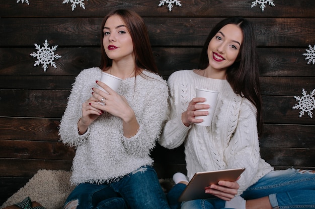 Zwei Frauen trinken ein heißes Getränk und schauen sich etwas auf einer Tablette an