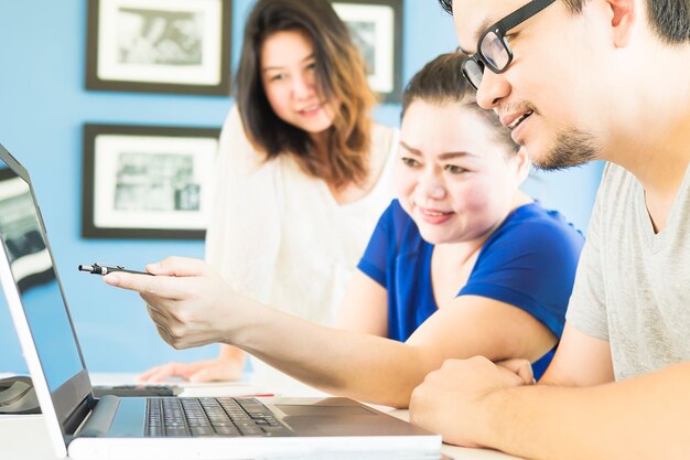 Zwei Frauen und ein Mann betrachten glücklich Computer im modernen Büro