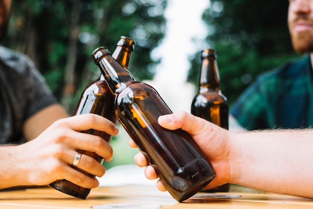 Kostenloses Foto zwei freunde, die die flaschen bier über der tabelle klirren