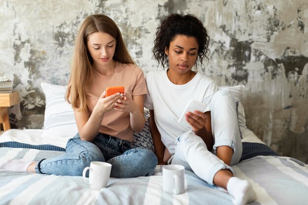 Zwei Freundinnen, die Smartphones im Bett betrachten