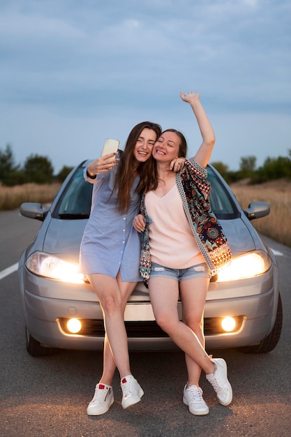 Zwei Freundinnen machen ein Selfie, während sie sich gegen das Auto lehnen