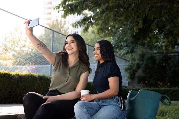 Zwei Freundinnen machen Selfie im Park, während sie einen Kaffee trinken