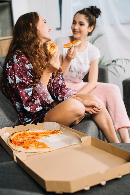 Kostenloses Foto zwei freundinnen mit scheibe der pizza einander betrachtend