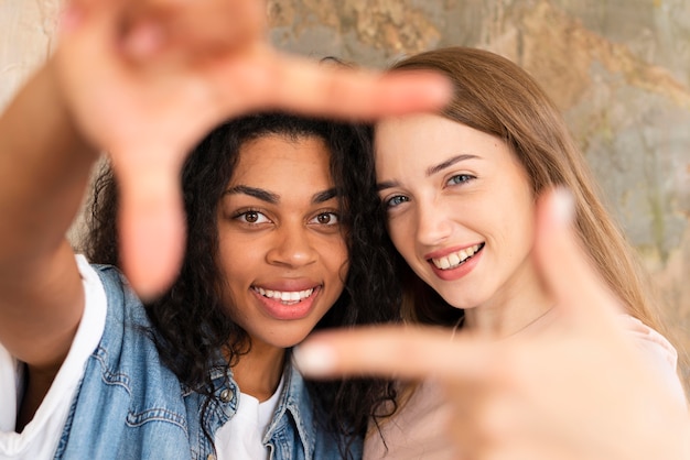 Zwei Freundinnen posieren beim Bilden des Rahmens mit den Fingern