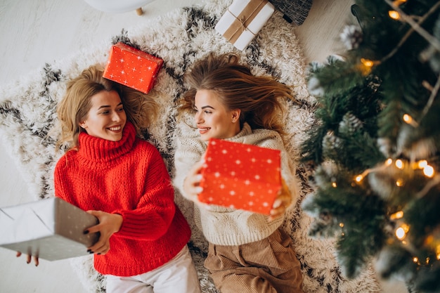 Zwei Freundinnen sitzen mit Weihnachtsgeschenken am Baum