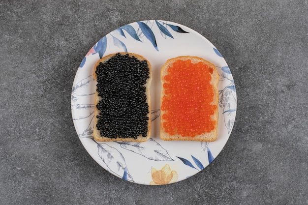 Zwei frische Sandwiches mit rotem und schwarzem Kaviar auf Platte über grauer Oberfläche.