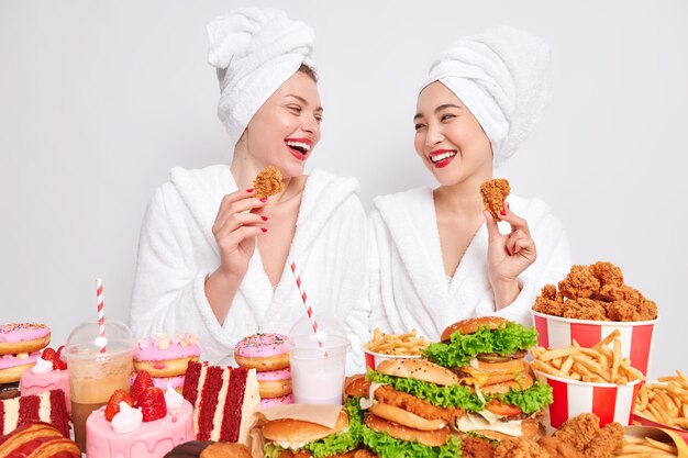 Zwei fröhliche diverse Frauen schauen sich gerne an halten Nuggets essen leckeres Fast Food fast