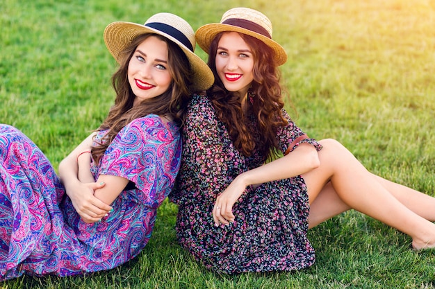 zwei fröhliche Zwillinge sitzen auf grüner Wiese und genießen die Zeit zusammen.
