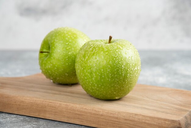 Zwei ganze grüne Äpfel auf Holzplatte auf Marmortisch.