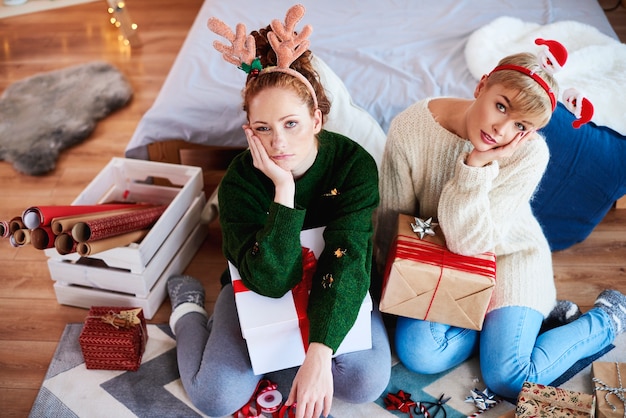 Zwei gelangweilte Mädchen, die Weihnachtsgeschenke für Weihnachten vorbereiten