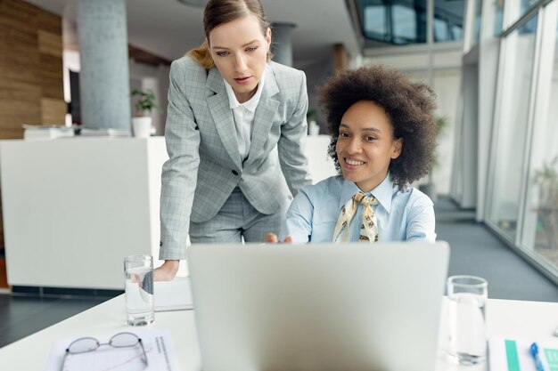 Zwei Geschäftsfrauen arbeiten zusammen, während sie im Büro am Laptop arbeiten