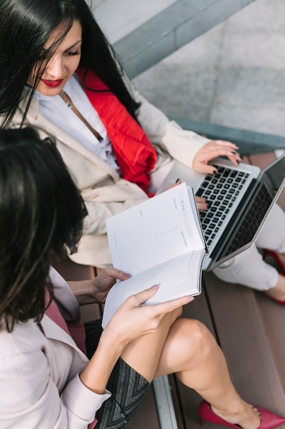 Zwei Geschäftsfrauen, die auf dem Treppenhaus betrachtet Tagebuch sitzen und Laptop verwenden