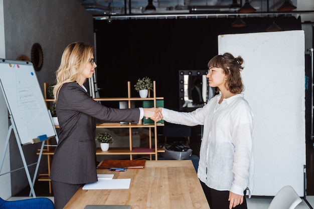 Kostenloses Foto zwei geschäftsfrauen, die hände im büro rütteln