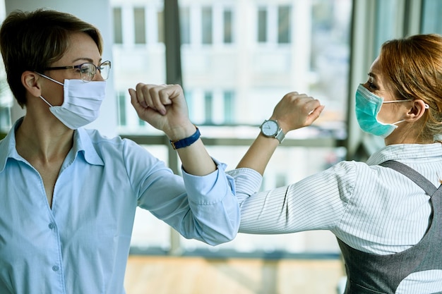 Zwei Geschäftsfrauen stoßen während der COVID19-Epidemie an den Ellbogen, während sie sich im Büro begrüßen