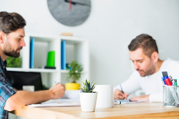 Zwei Geschäftsmänner, die über hölzernem Schreibtisch am Arbeitsplatz arbeiten