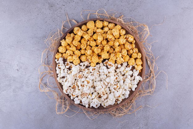 Zwei Geschmacksrichtungen von Popcorn, serviert auf einem Holztablett, das mit Stroh auf Marmorhintergrund dekoriert ist. Foto in hoher Qualität
