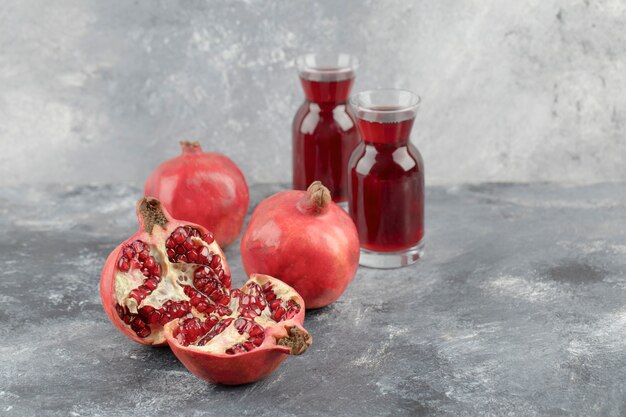 Zwei Gläser frischer Saft mit reifen Granatapfelfrüchten auf Marmoroberfläche.