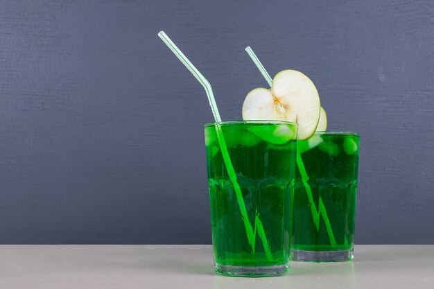 Zwei Gläser grüner Saft mit Strohhalmen auf blauem Tisch.