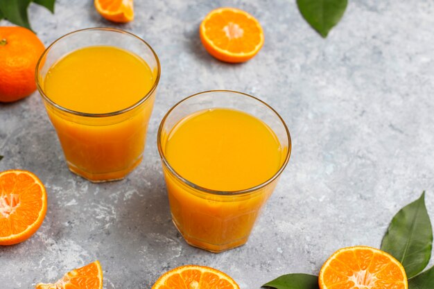 Zwei Gläser organischer frischer Orangensaft mit rohen Orangen, Mandarinen