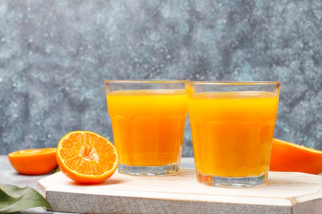 Zwei Gläser organischer frischer Orangensaft mit rohen Orangen, Mandarinen