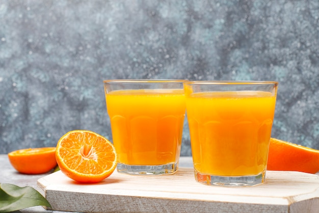 Zwei Gläser organischer frischer Orangensaft mit rohen Orangen, Mandarinen