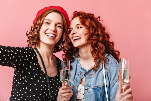 Zwei glamouröse Mädchen halten Weingläser und machen Selfie. Blithesome Damen, die Champagner genießen und positive Gefühle ausdrücken.
