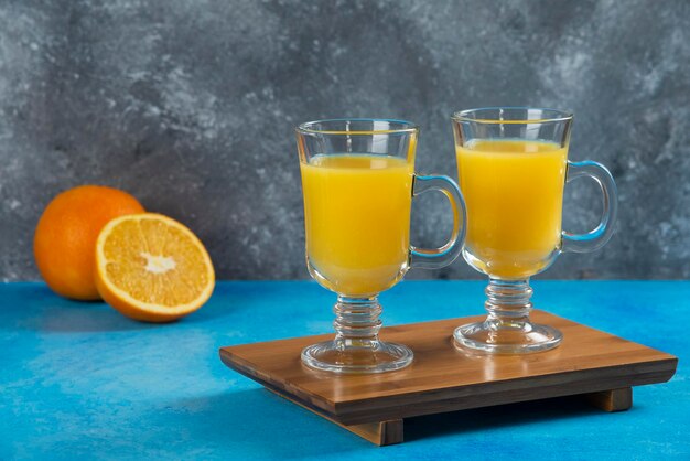 Zwei Glasbecher Orangensaft auf Holzbrett.