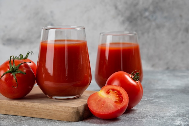 Zwei Glasbecher Tomatensaft auf einem Holzbrett.