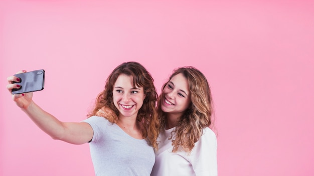 Zwei glückliche Freunde, die Selbstporträt auf dem Mobiltelefon steht gegen rosa Hintergrund nehmen