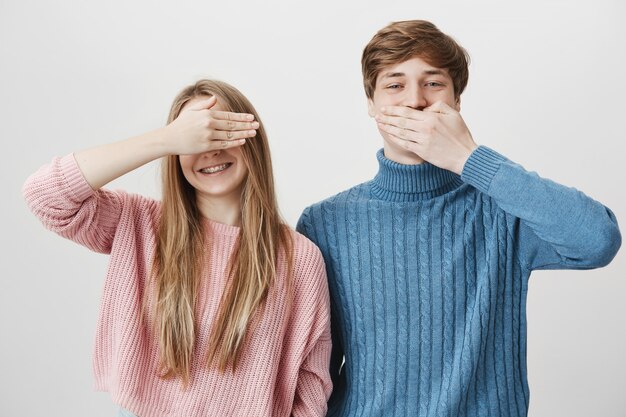 Zwei glückliche Geschwister, die Spaß haben. Mädchen bedecken Augen und Kerl schließen Mund, lachend