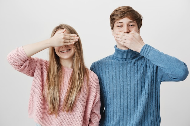 Zwei glückliche Geschwister, die Spaß haben. Mädchen bedecken Augen und Kerl schließen Mund, lachend